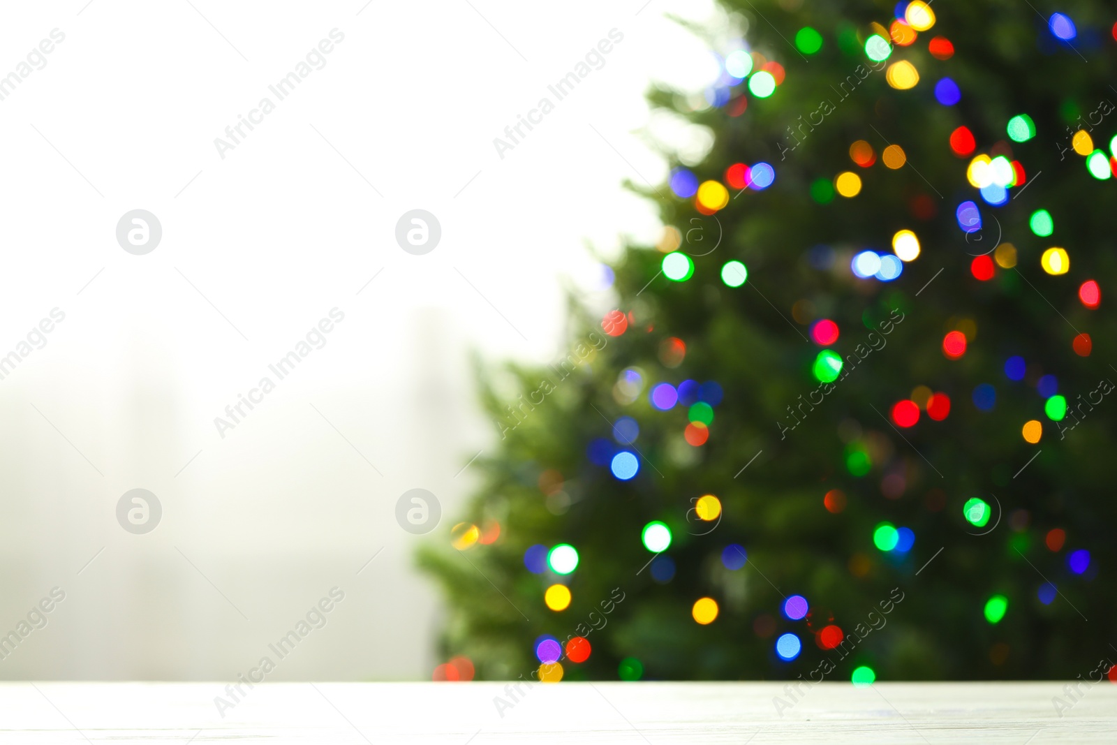 Photo of Empty table and blurred fir tree with colorful Christmas lights on background, bokeh effect. Space for design