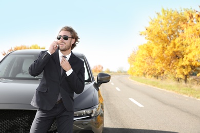 Photo of Young businessman talking on phone near modern car, outdoors