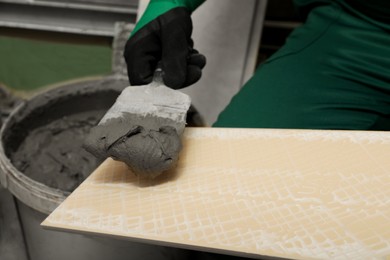 Photo of Worker applying adhesive mix on ceramic tile with spatula, closeup