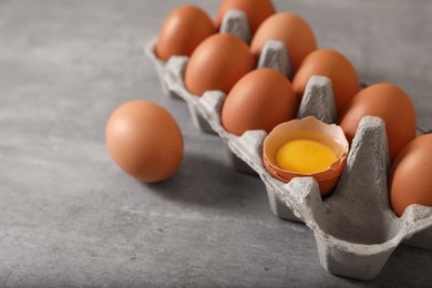 Fresh raw chicken eggs in carton on grey table, closeup