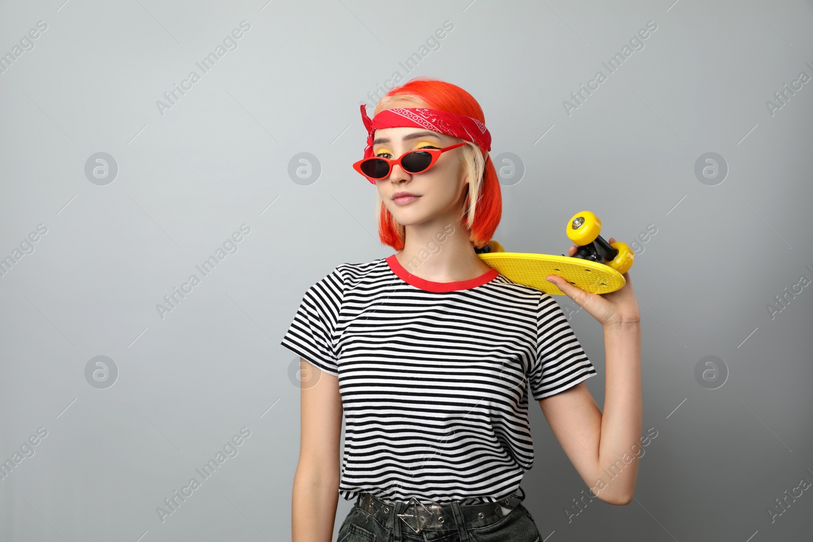 Photo of Beautiful young woman with bright dyed hair holding skateboard on light grey background