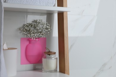 Silicone vase with flowers on white marble wall and shelving unit in stylish bathroom. Space for text