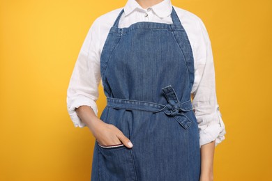 Photo of Young woman in blue jeans apron on yellow background, closeup