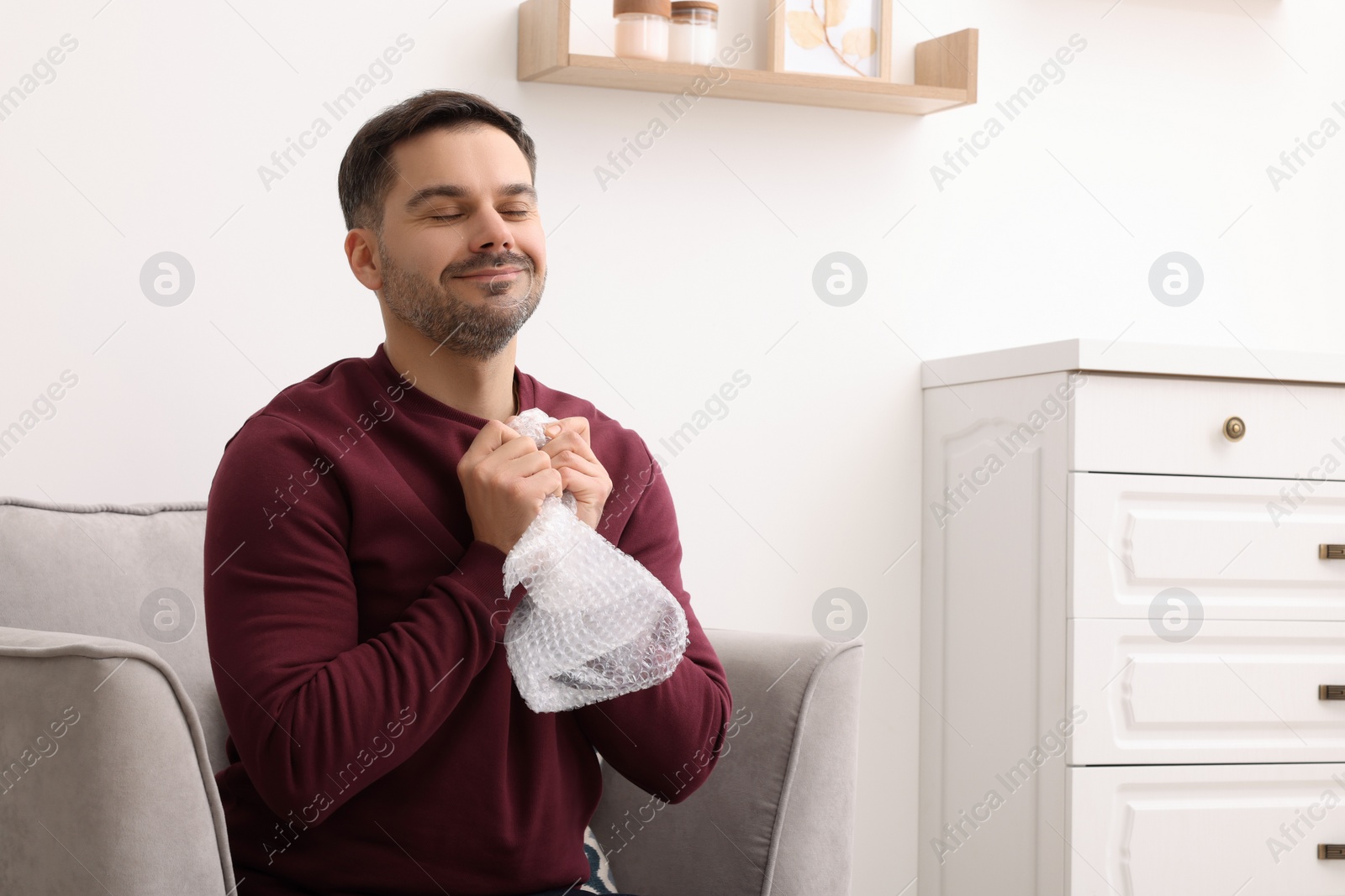 Photo of Happy man with bubble wrap indoors. Space for text