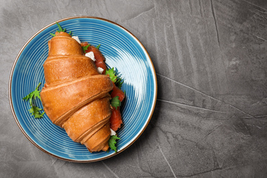 Tasty croissant sandwich with red fish on grey table, top view. Space for text