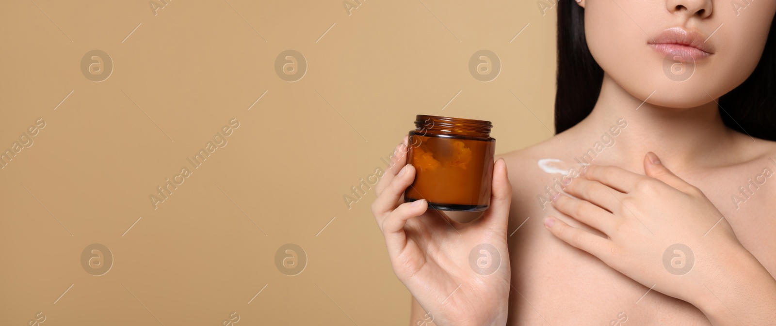 Photo of Beautiful young Asian woman with jar of body cream on beige background, closeup