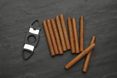 Cigars and guillotine cutter on black table, flat lay