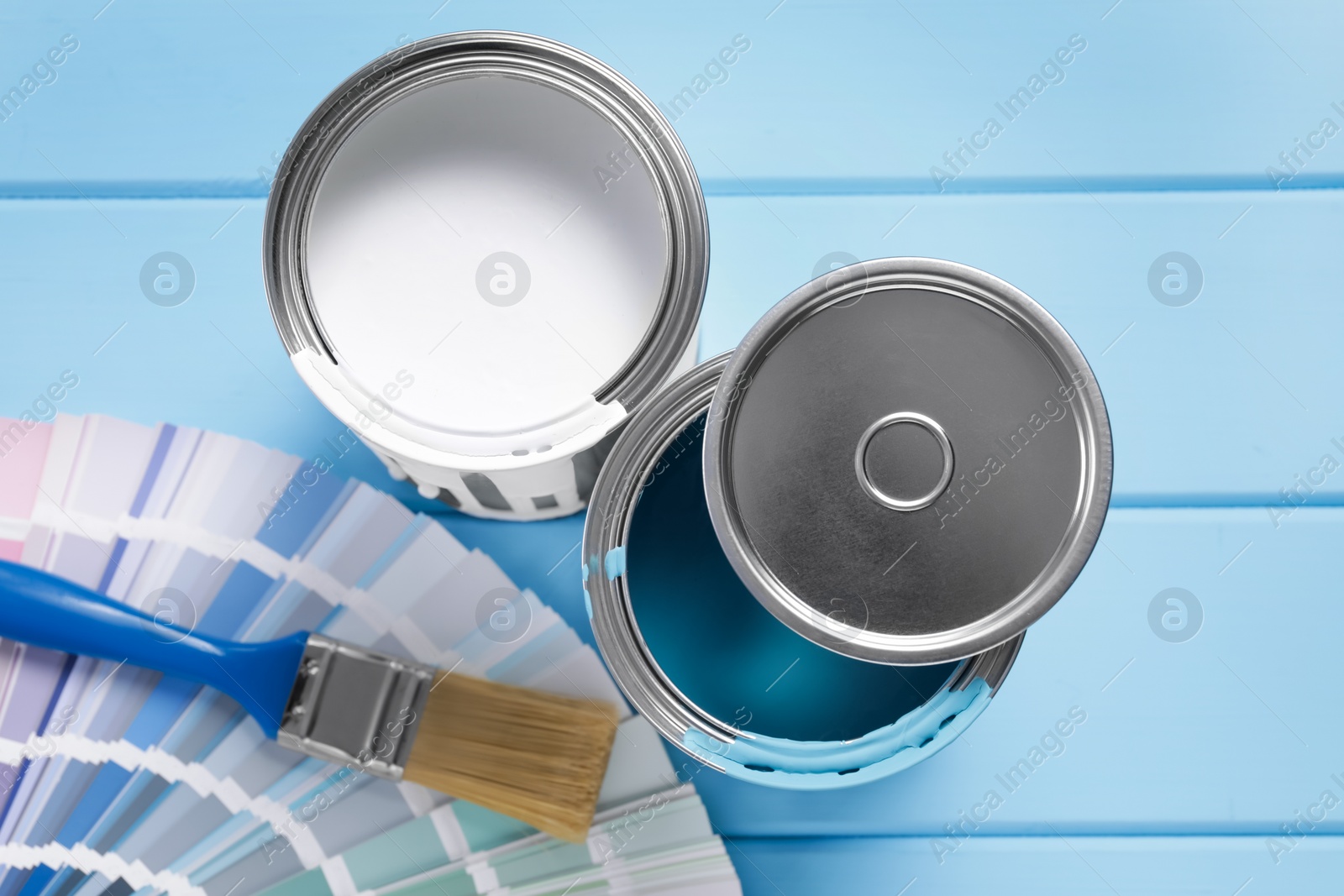 Photo of Cans of paints, brush and palette on light blue wooden table