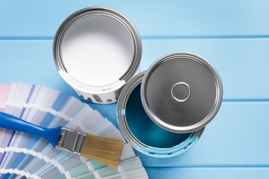 Photo of Cans of paints, brush and palette on light blue wooden table