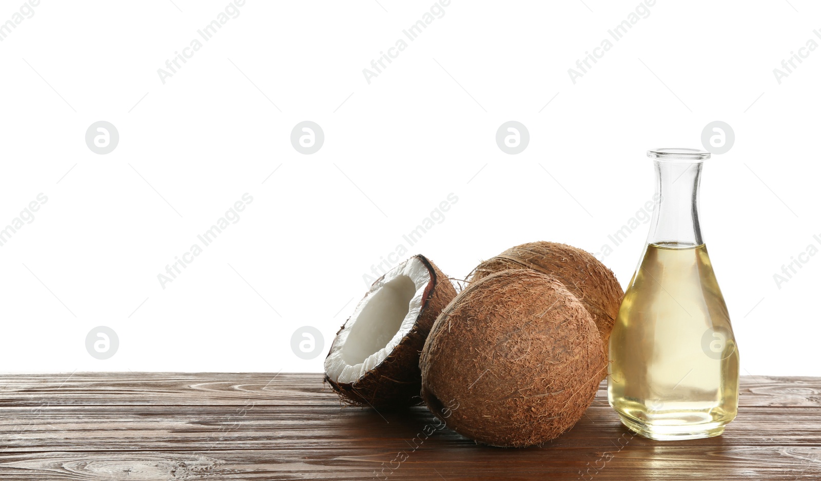Photo of Ripe coconuts and bottle with natural organic oil on wooden table against white background