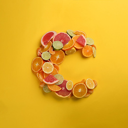 Photo of Letter C made with citrus fruits on yellow background as vitamin representation, flat lay