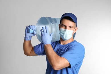 Courier in face mask with bottle of cooler water on grey background. Delivery during coronavirus quarantine