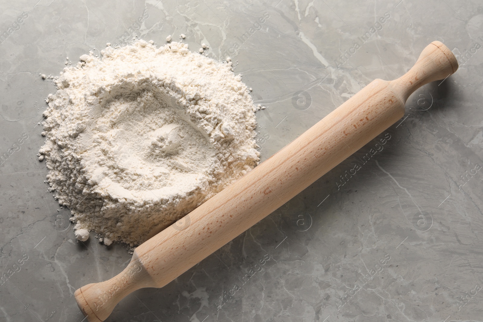 Photo of Pile of flour and rolling pin on grey marble table, top view