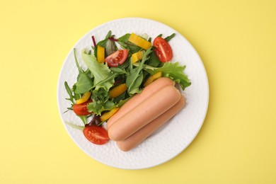 Photo of Delicious boiled sausages with salad on yellow background, top view