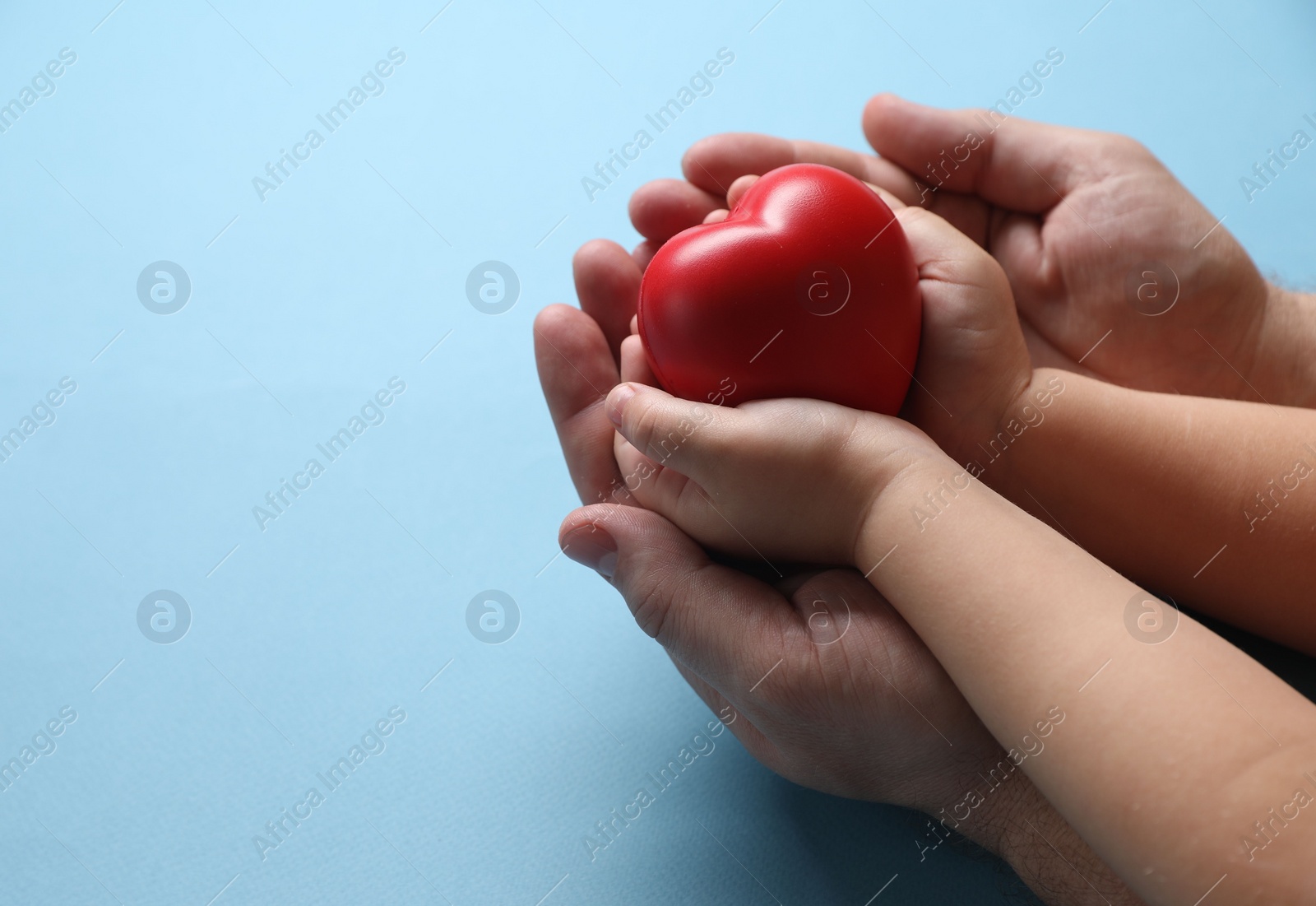 Photo of Father and his child holding red decorative heart on light blue background, closeup. Space for text
