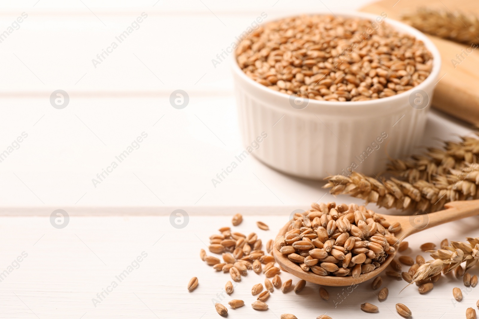 Photo of Wheat grains on white wooden table, space for text