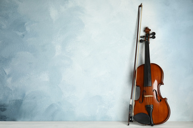 Photo of Beautiful violin and bow on white wooden table near light blue wall. Space for text