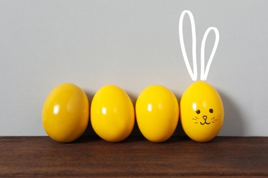 One egg with drawn face and ears as Easter bunny among others on wooden table against light grey background