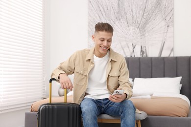 Photo of Smiling guest with smartphone and suitcase in stylish hotel room