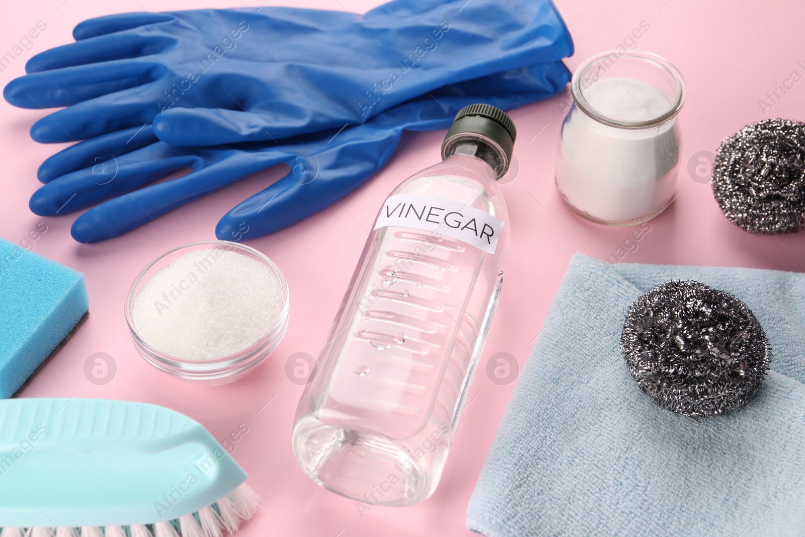 Photo of Eco friendly natural cleaners. Vinegar in bottle, soda, brushes and gloves on pink background