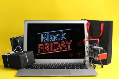 Photo of Laptop with Black Friday announcement, small shopping cart and gifts on yellow background
