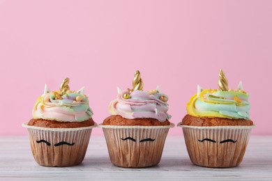 Photo of Cute sweet unicorn cupcakes on white wooden table against pink background
