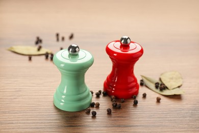 Photo of Salt and pepper shakers with bay leaves on wooden table, closeup. Spice mill