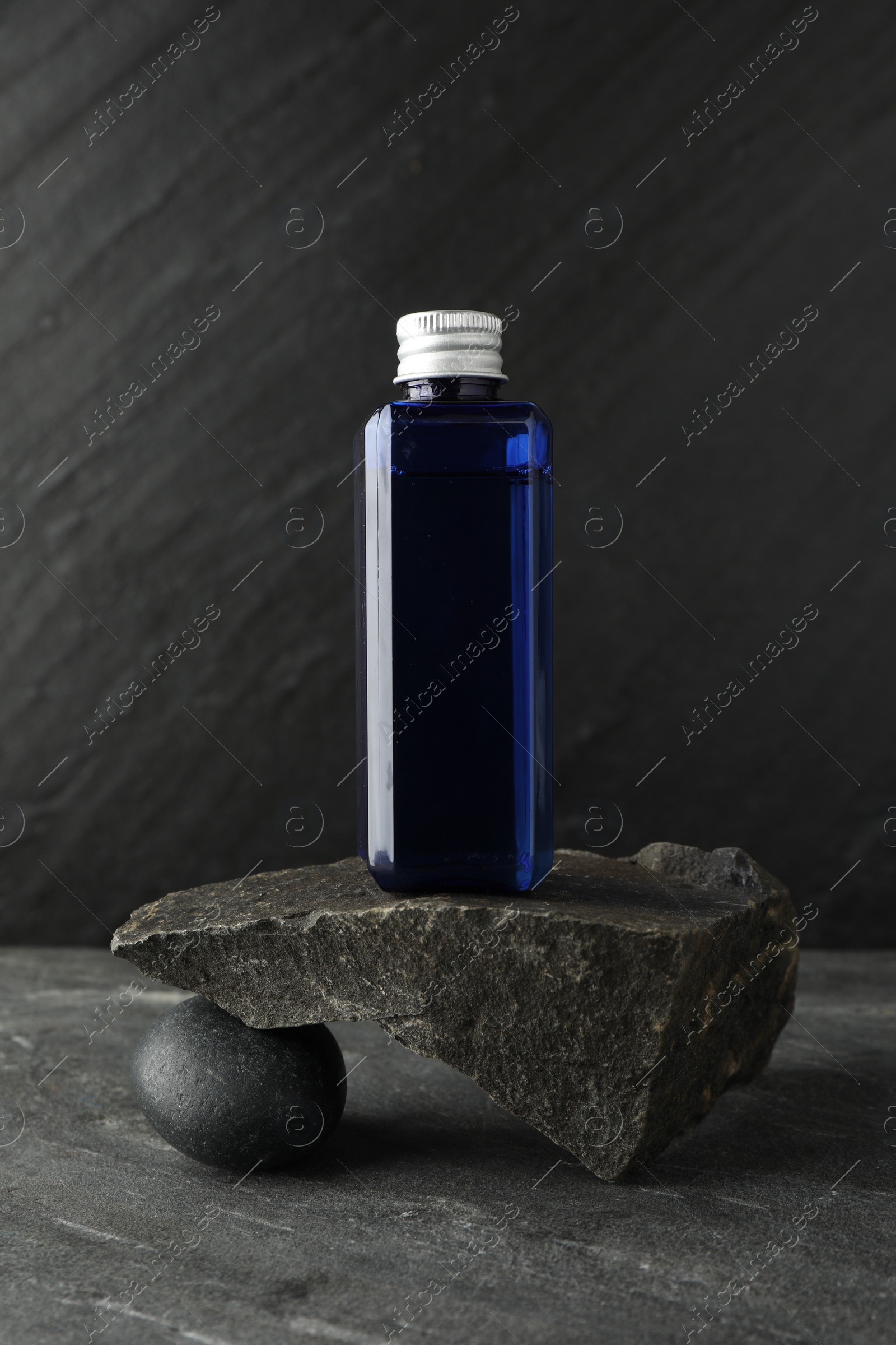 Photo of Bottle of cosmetic product and stones on light grey background