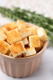 Delicious crispy croutons in bowl on white marble table, closeup