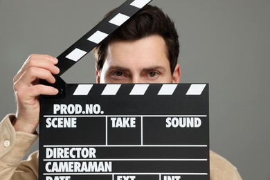 Actor holding clapperboard on grey background, closeup