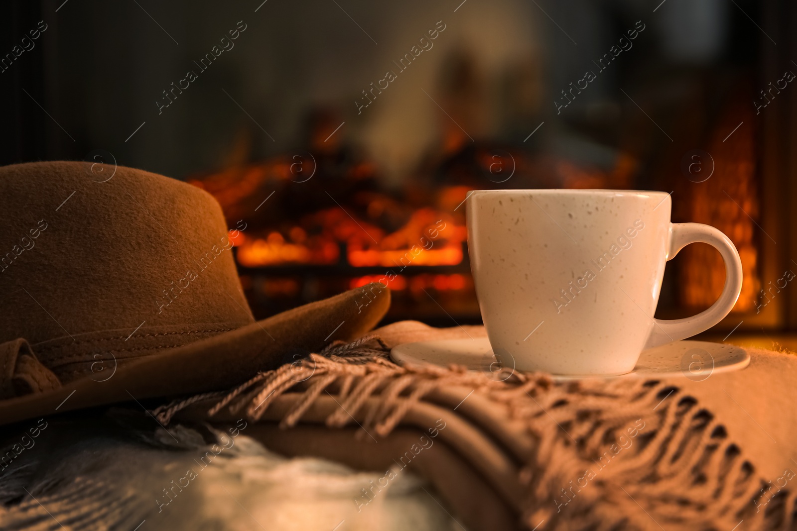 Photo of Cup with hot drink and hat on plaids against fireplace