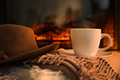 Cup with hot drink and hat on plaids against fireplace