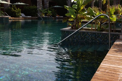 Swimming pool, metal rail and tropical plants at luxury resort