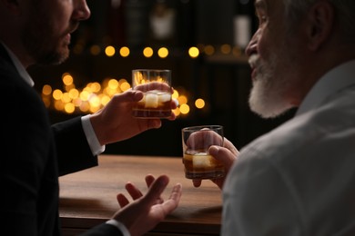 Men with glasses of whiskey talking at wooden table in bar