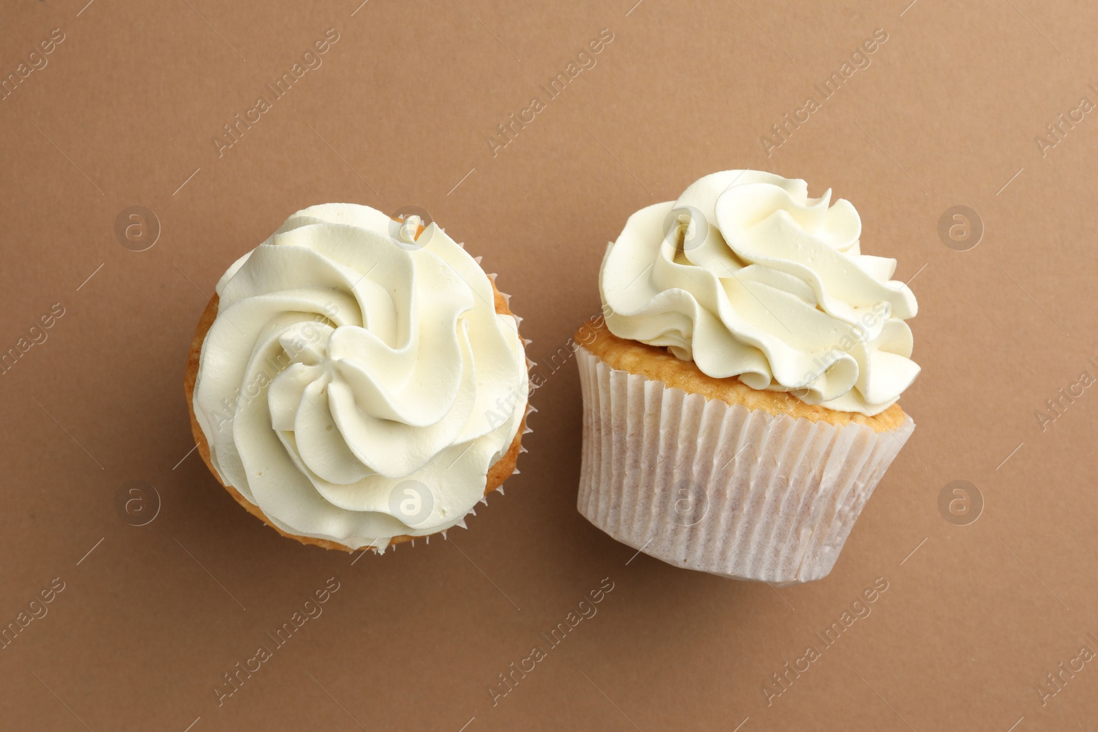 Photo of Tasty vanilla cupcakes with cream on dark beige background, top view