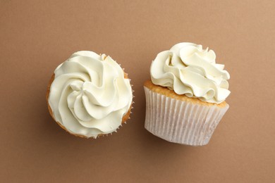 Photo of Tasty vanilla cupcakes with cream on dark beige background, top view