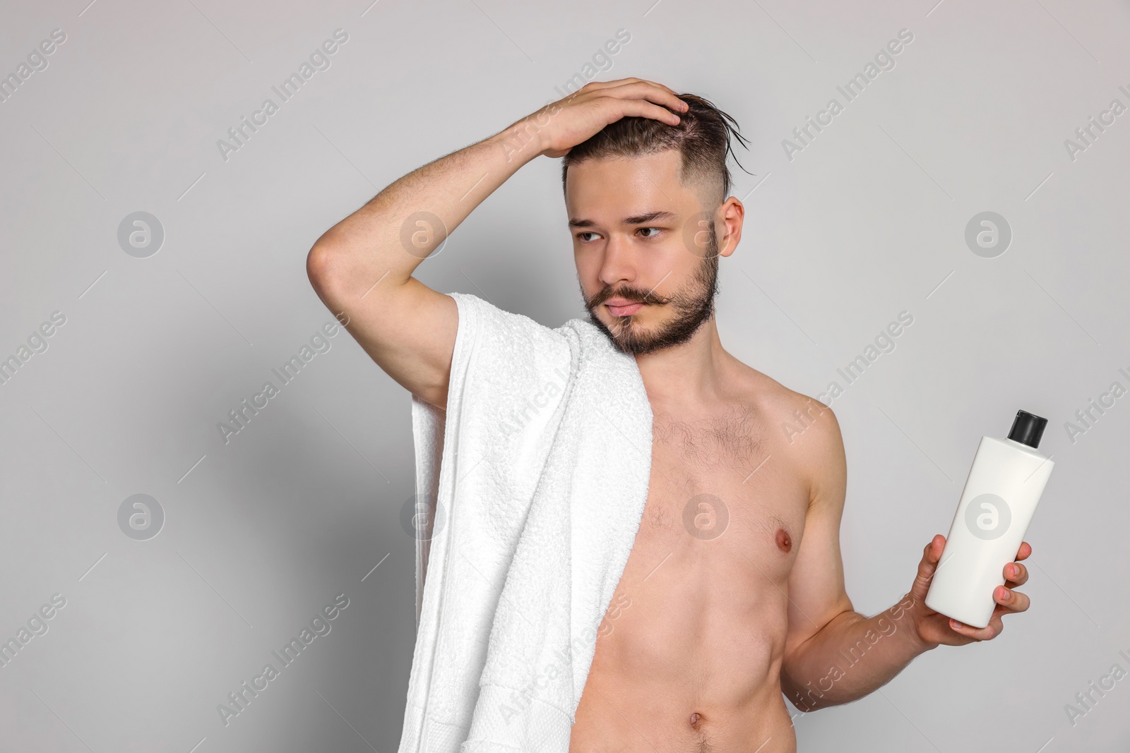 Photo of Naked man with towel and bottle of shampoo on light grey background