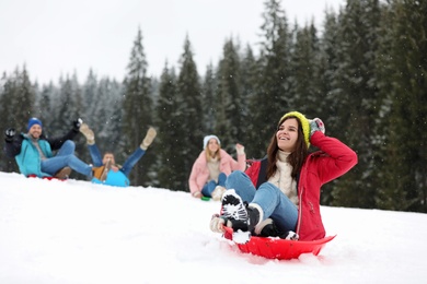 Happy friends sliding on sleds outdoors. Winter vacation