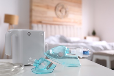 Photo of Modern nebulizer with face masks on white table indoors, space for text. Inhalation equipment