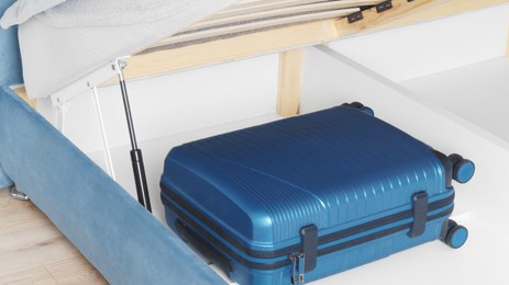 Storage drawer under bed with blue suitcase indoors