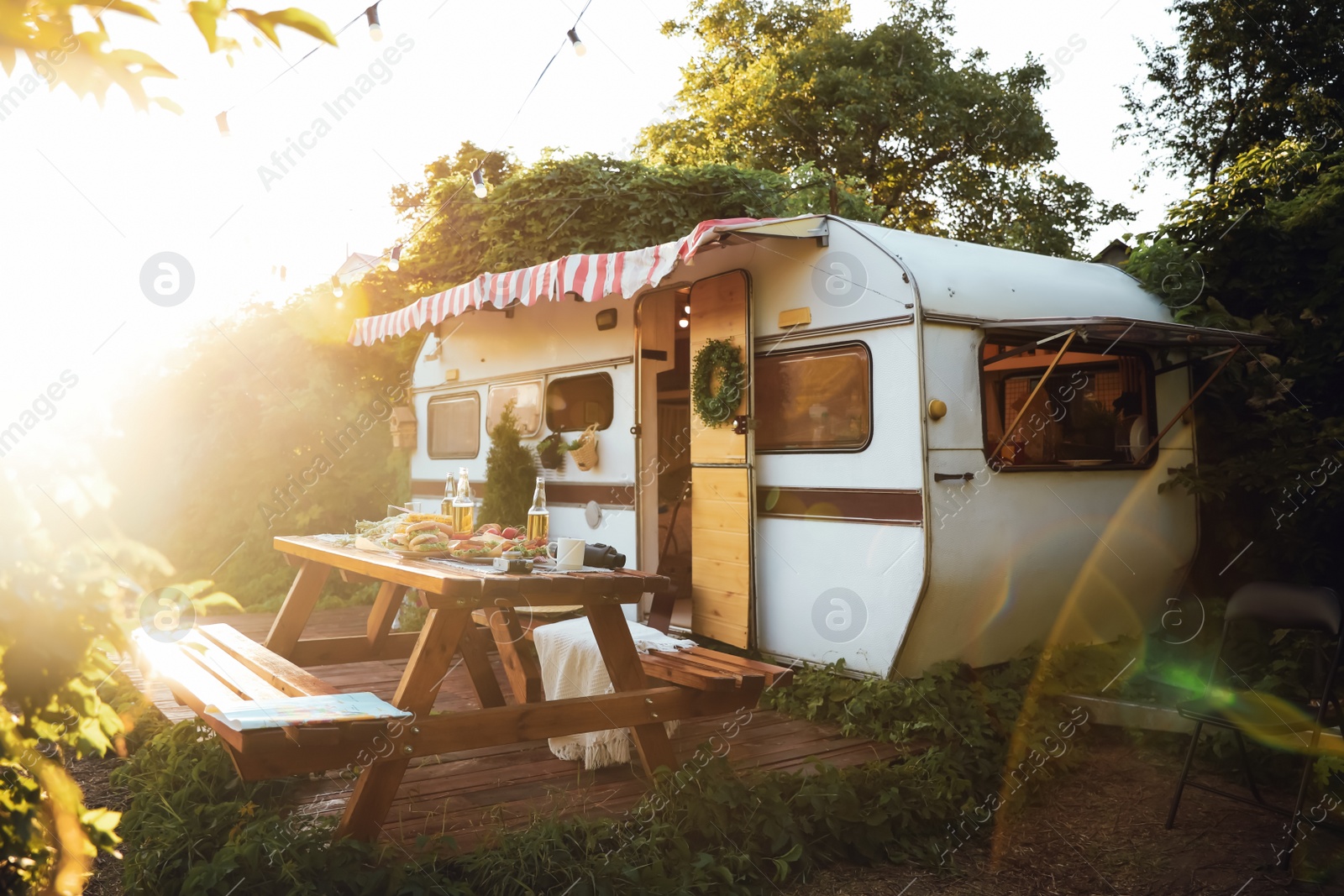 Photo of Wooden table with food and drinks of beer near trailer on sunny day. Camping season