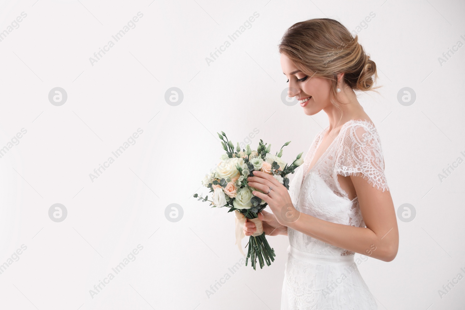 Photo of Young bride with elegant hairstyle holding wedding bouquet on white background