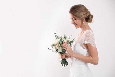 Photo of Young bride with elegant hairstyle holding wedding bouquet on white background
