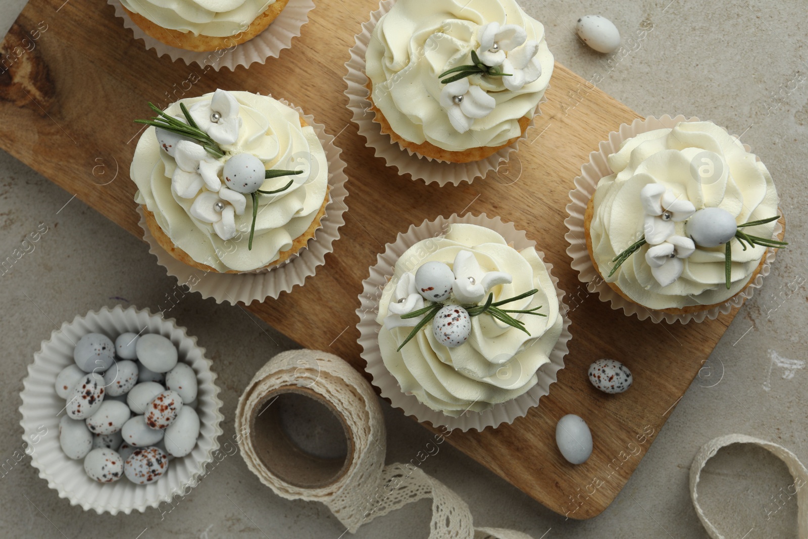 Photo of Tasty Easter cupcakes with vanilla cream, candies and ribbon on gray table, flat lay