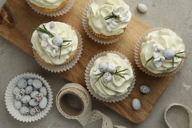 Photo of Tasty Easter cupcakes with vanilla cream, candies and ribbon on gray table, flat lay