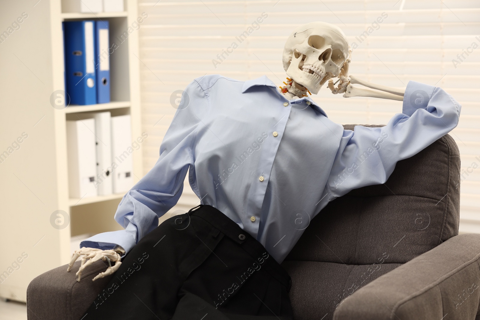 Photo of Waiting concept. Human skeleton sitting in armchair at office