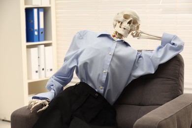 Waiting concept. Human skeleton sitting in armchair at office