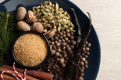 Plate with different aromatic spices and fir branches on light wooden table, top view