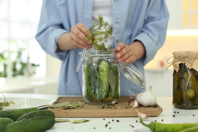 Photo of Woman putting dill into pickling jar at table in kitchen, closeup