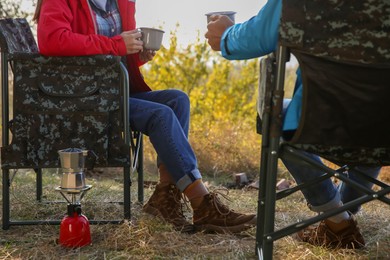 Photo of Couple resting in camping chairs and enjoying hot drink outdoors, closeup